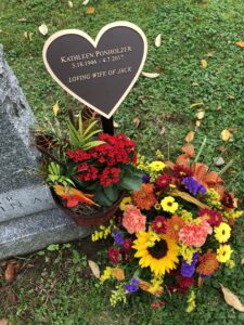 Heart-shaped bronze memorial plaque with engraved tribute and flower display at gravesite